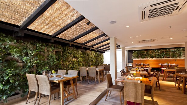A restaurant with wooden tables and chairs, a checkered floor, and a wall with green plants.