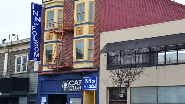 A building with a blue and yellow facade, a sign for 'Cat Club', and a 'Inn on Folsom' banner. - Inn on Folsom (San Francisco)
