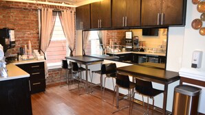 A modern kitchen with a brick wall, wooden cabinets, and a bar area with stools. - Inn on Folsom (San Francisco)