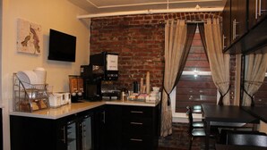 A kitchen with a brick wall, a coffee machine, and a dining area with a table and chairs. - Inn on Folsom (San Francisco)