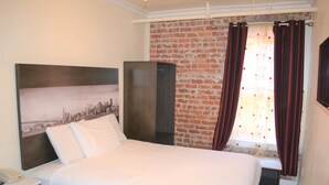 A hotel room with a bed, a wardrobe, a cityscape artwork on the wall, and a brick wall. - Inn on Folsom (San Francisco)