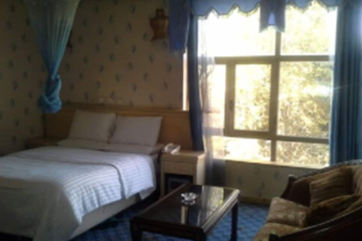 A bedroom with a bed, a nightstand, a glass-top table, and a sofa.