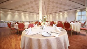 Een balzaal met ronde tafels gedekt voor een diner, een hoog plafond en een centrale pilaar.