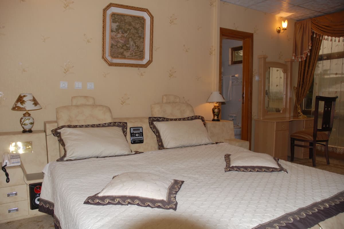 A hotel room with a large bed, two bedside tables, a nightstand, a chair, a mirror, and a painting on the wall.