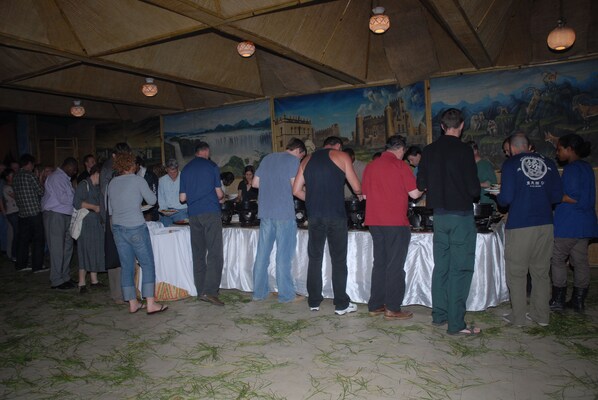 A group of people standing in a covered area with tables, possibly a dining or event space.