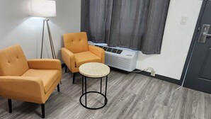 A room with two yellow armchairs, a small round table, a floor lamp, and a wall-mounted air conditioner. - Country Inn Banning (Banning)