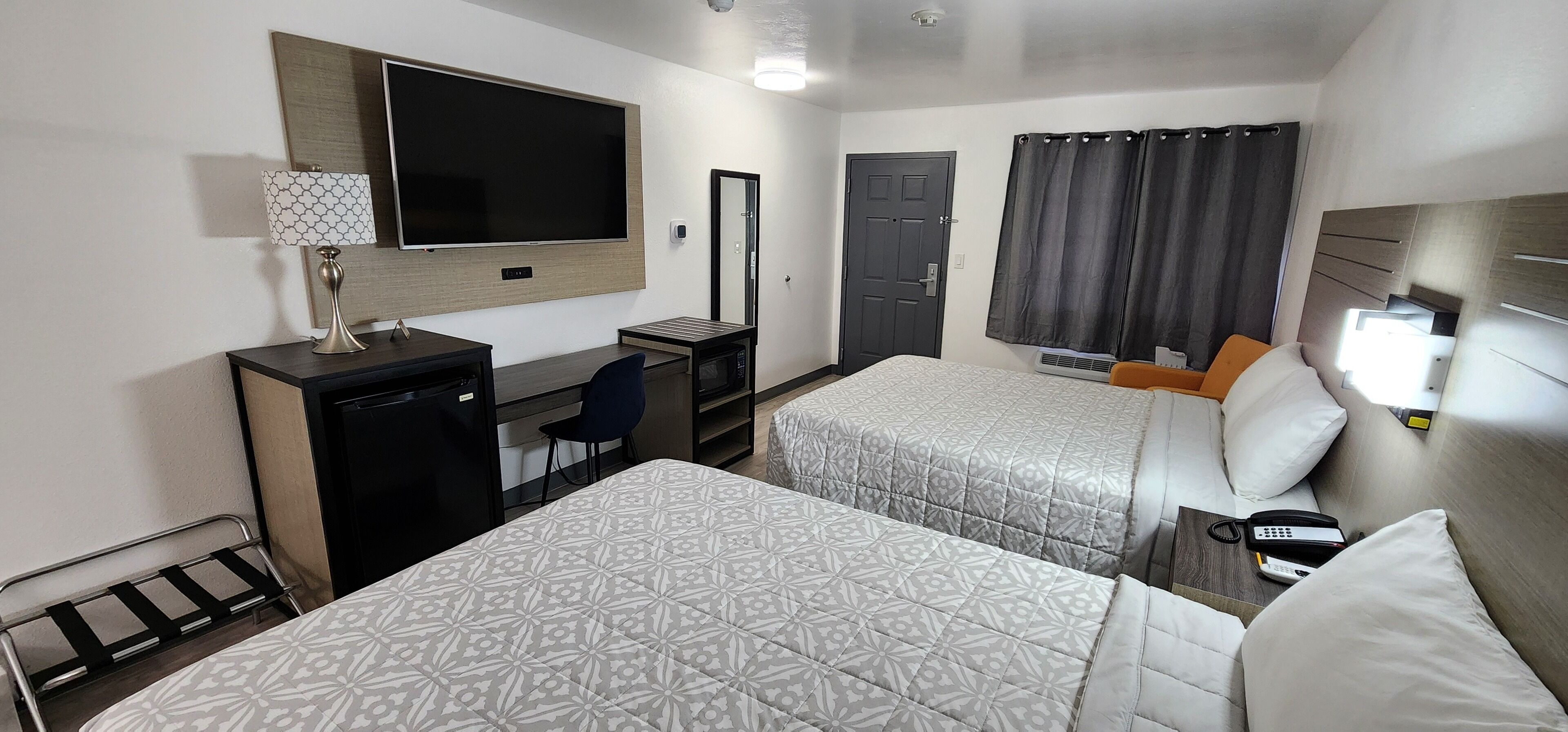 A hotel room with two beds, a desk with a computer, a TV, a mirror, a door, and a window with curtains.