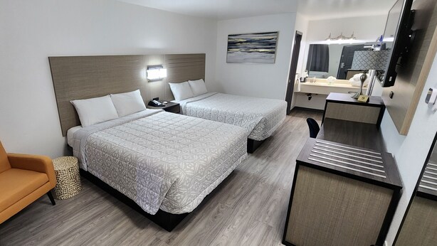 A hotel room with two beds, a sofa, a small table, a mirror, and a bathroom with a sink and mirror. - Country Inn Banning (Banning)