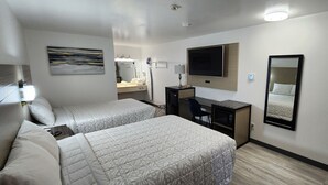 A hotel room with two beds, a desk, a TV, a mirror, and a shower area. - Country Inn Banning (Banning)
