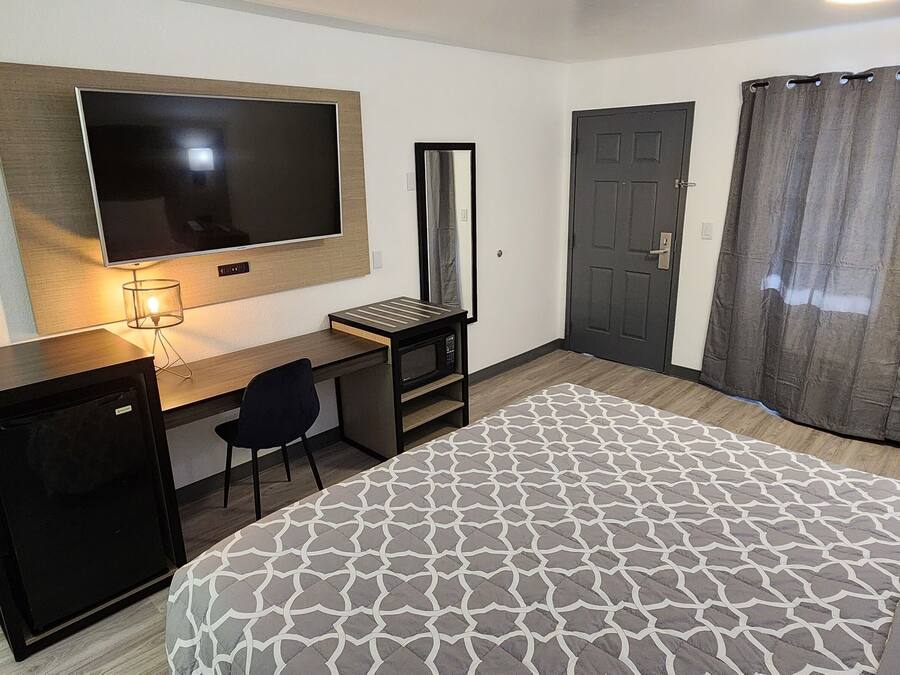A hotel room with a bed, a desk with a computer, a TV mounted on the wall, a door, and a shower curtain.