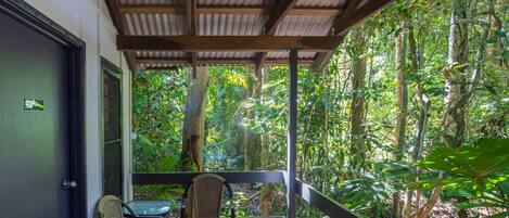 Un espacio al aire libre techado con mesa y sillas, rodeado de abundante follaje tropical.