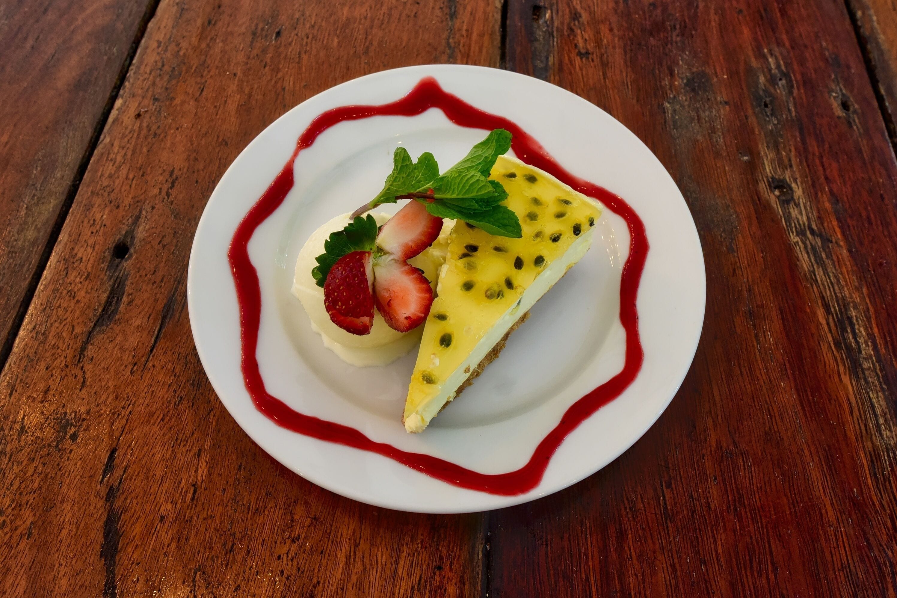 A dessert on a white plate with a red sauce border, placed on a wooden table.