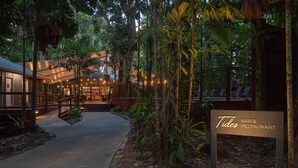 Un sendero conduce a un bar y restaurante llamado 'Tides', rodeado de exuberante vegetación y una estructura de edificio moderna.