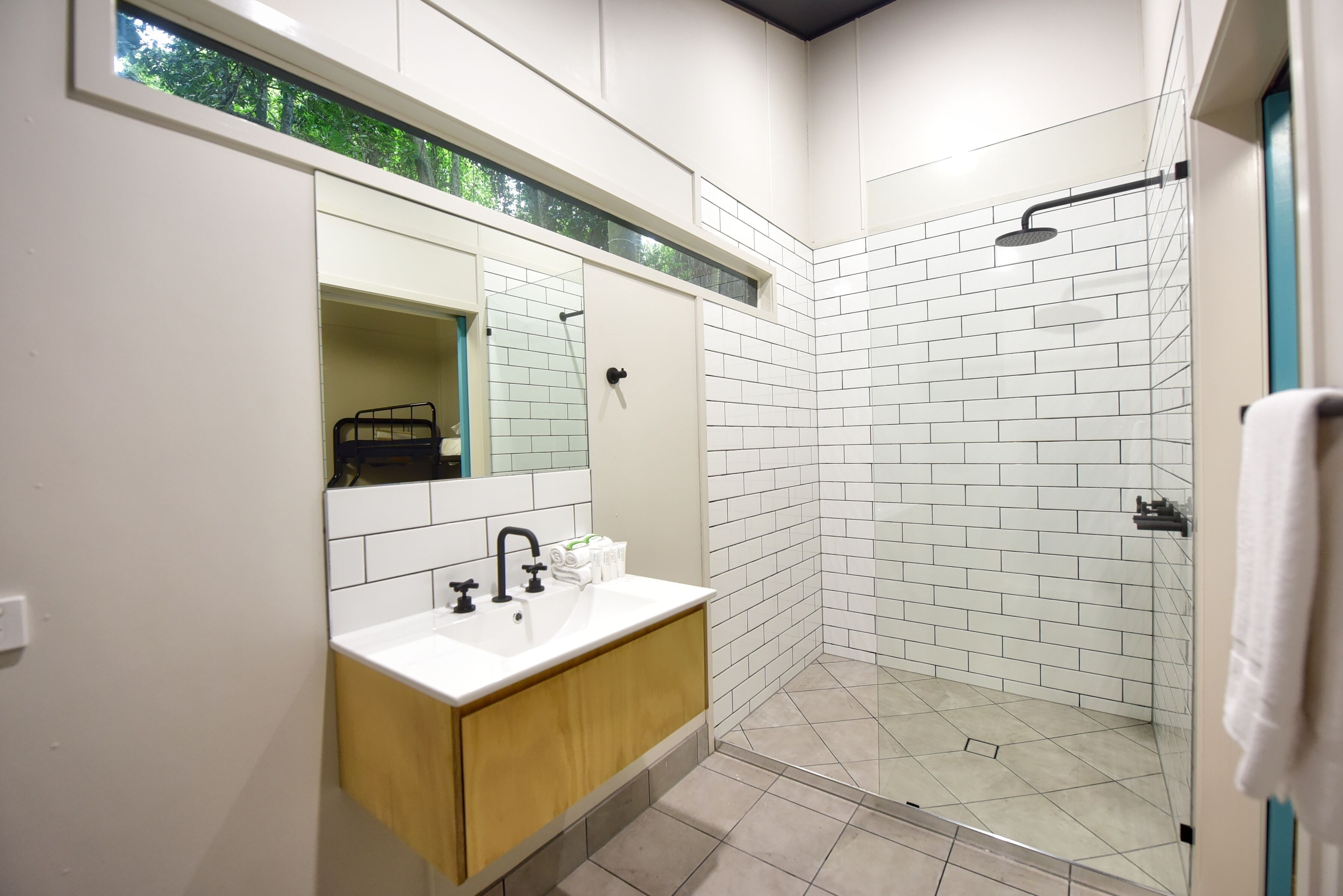 Un baño moderno con un lavamanos blanco, espejo y zona de ducha con azulejos blancos.