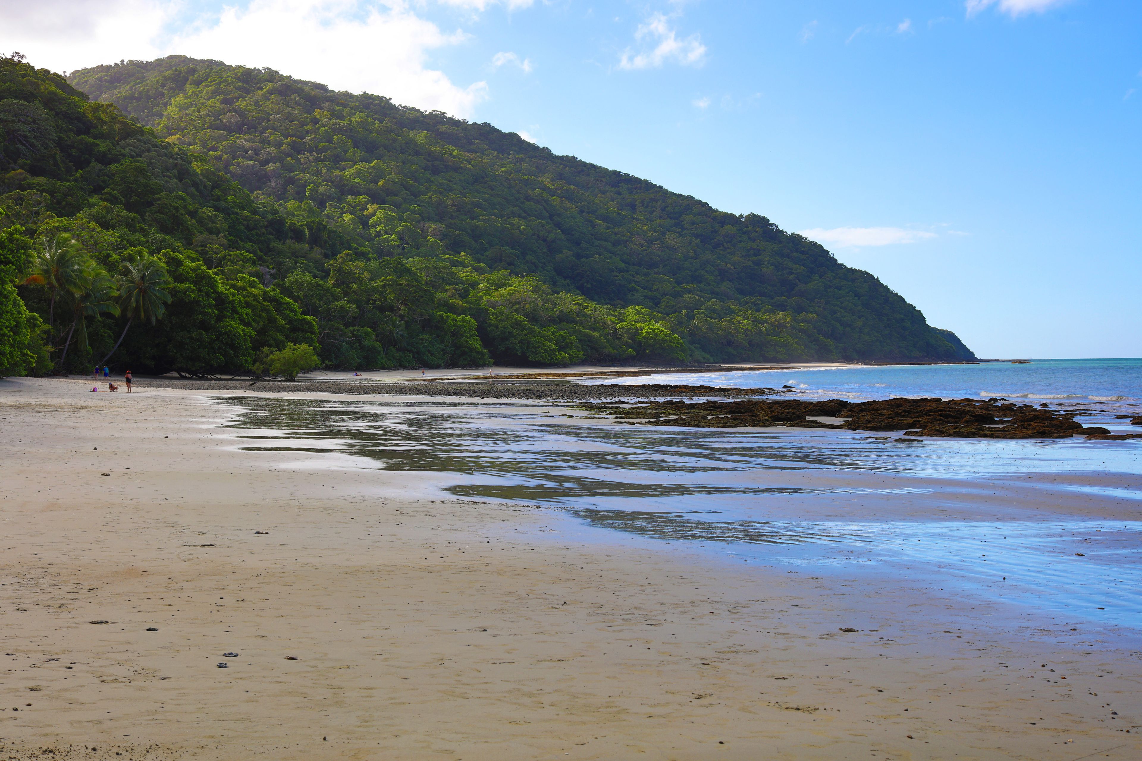 A beach with a sandy shore, a rocky outcrop, and a forested hill in the background.