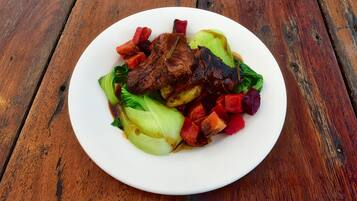 A plate of food with meat, vegetables, and a white plate on a wooden table.