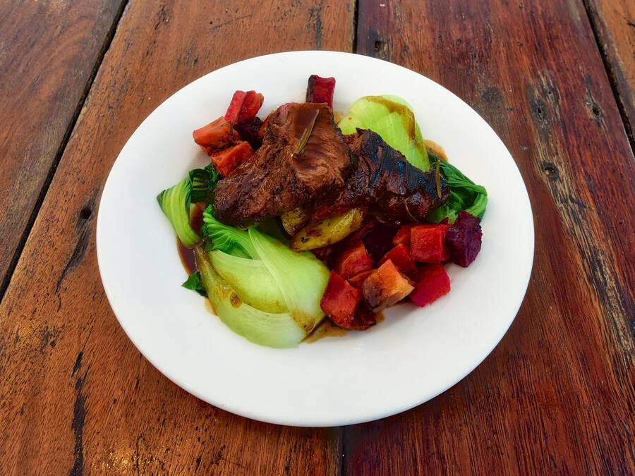 A plate of food with meat, vegetables, and a white plate on a wooden table.
