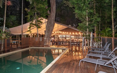 A pool area with lounge chairs, a wooden deck, and a covered seating area with string lights.
