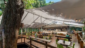 Un restaurante al aire libre con mesas en terraza de madera, sombrillas grandes y una zona de bar.