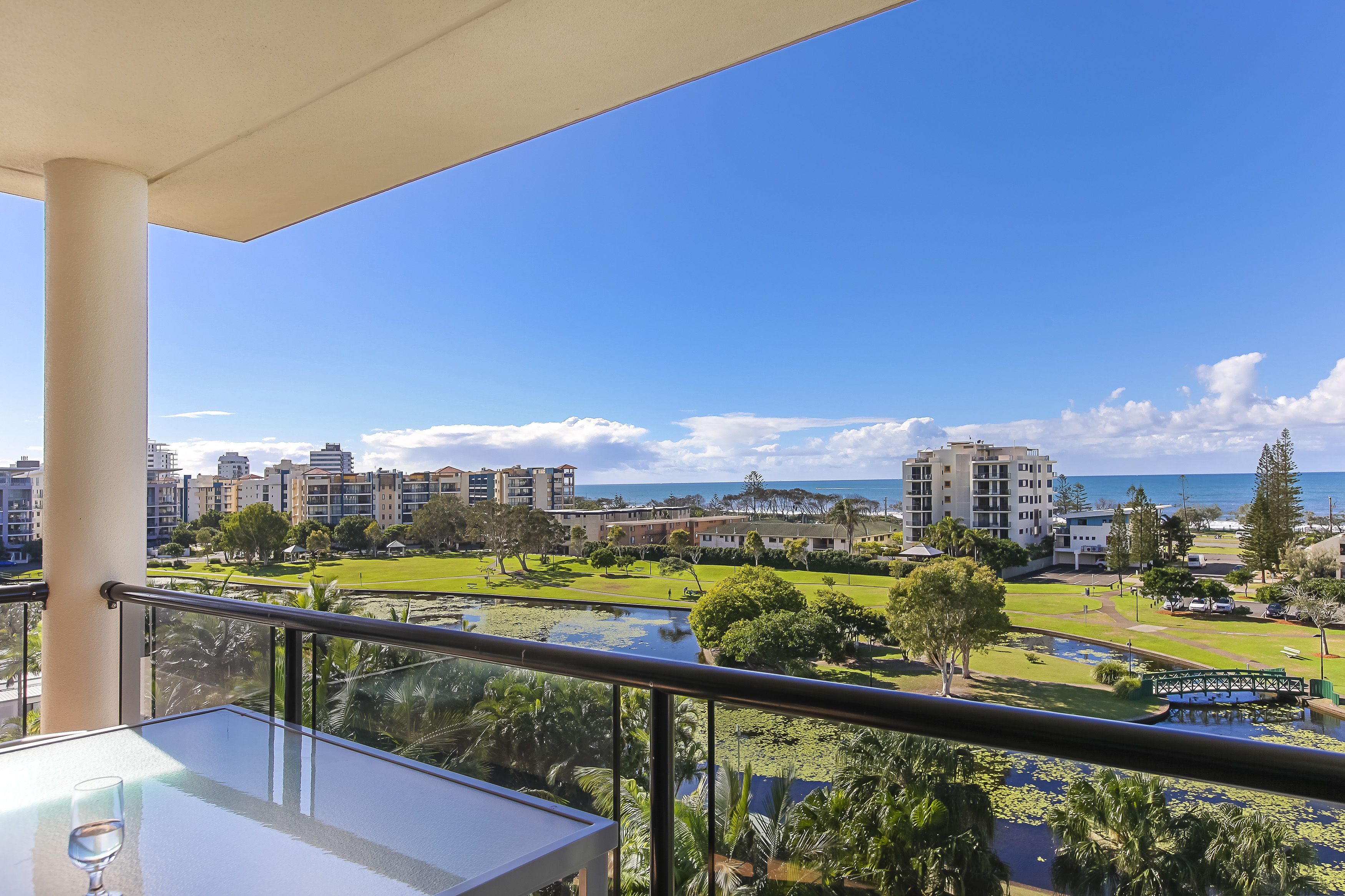 A balcony with a clear view of a landscaped area, a pond, and buildings in the background.