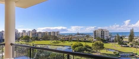 A balcony with a clear view of a landscaped area, a pond, and buildings in the background.