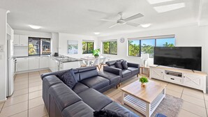 A modern living room with a sectional sofa, a flat-screen TV, and a dining area with a table and chairs. - The Mirage Alexandra Headland (Alexandra Headland)