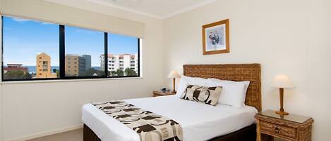 Hotelkamer met een groot bed, een plafondventilator, een raam met uitzicht op de stad en een ingelijst schilderij aan de muur.