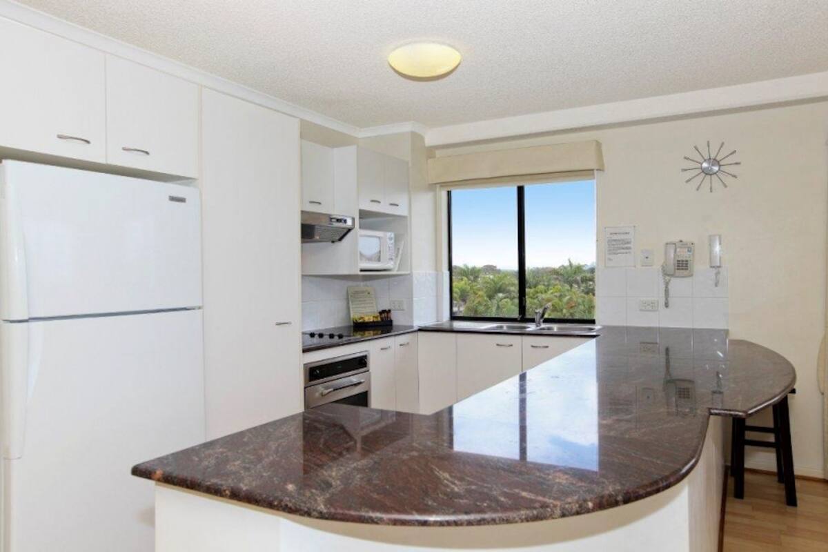 A modern kitchen with white cabinets, a built-in microwave, a stove, and a large window offering a view of greenery.