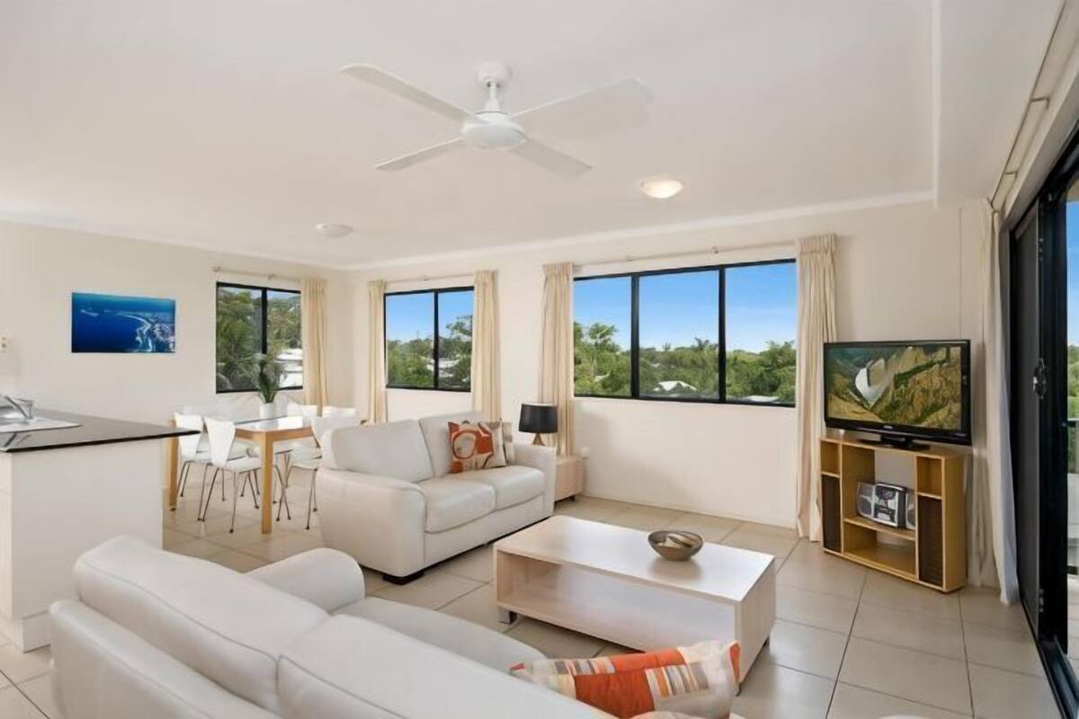 A modern living room with a sofa, coffee table, TV, and dining area.
