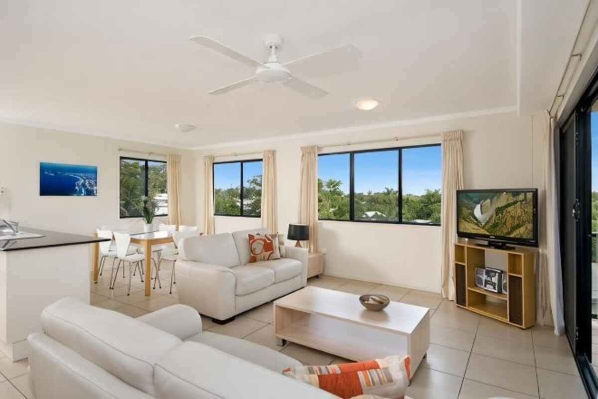 A modern living room with a sofa, coffee table, TV, and dining area.