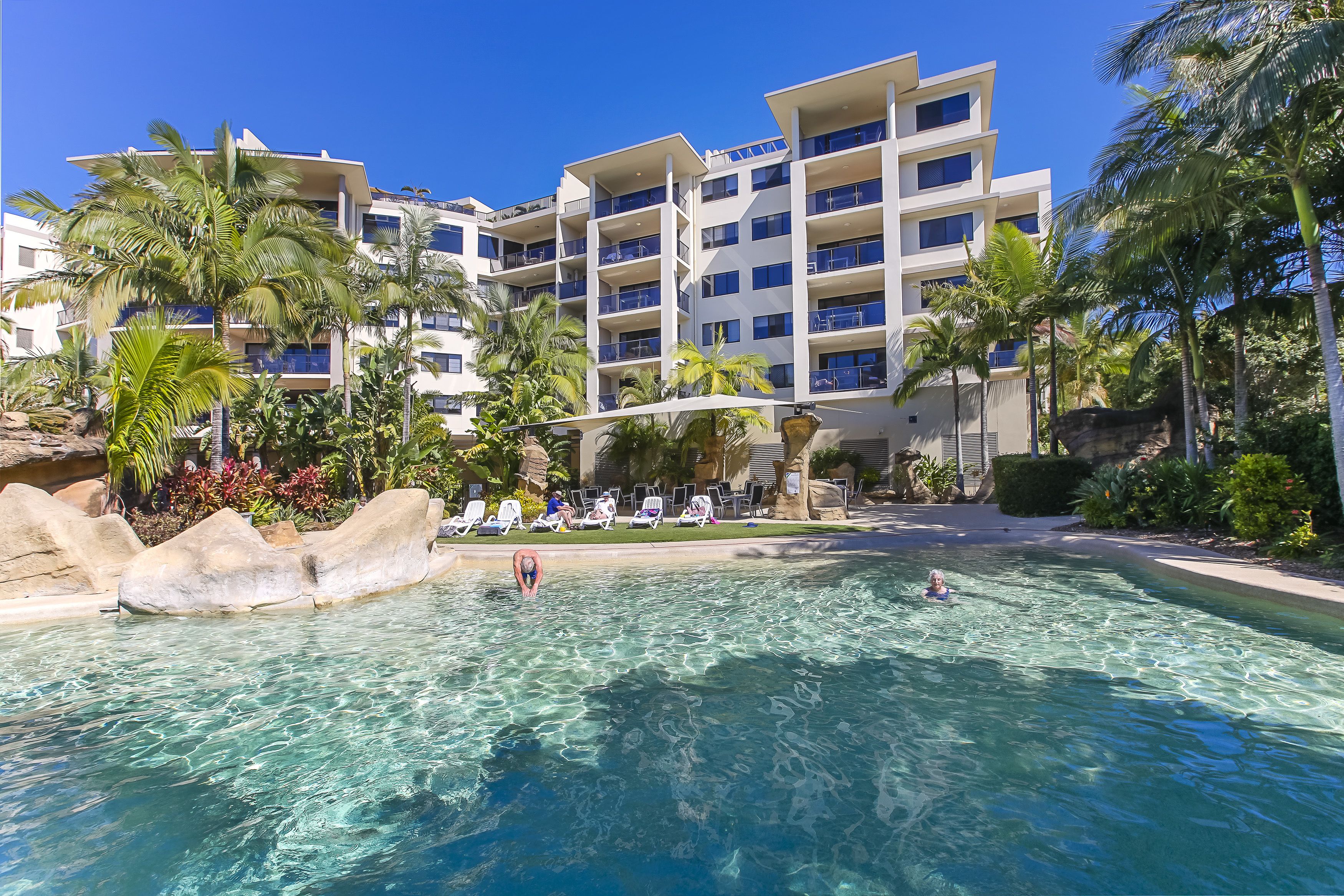 Un hotel con piscina rodeado de palmeras y un cielo azul despejado.