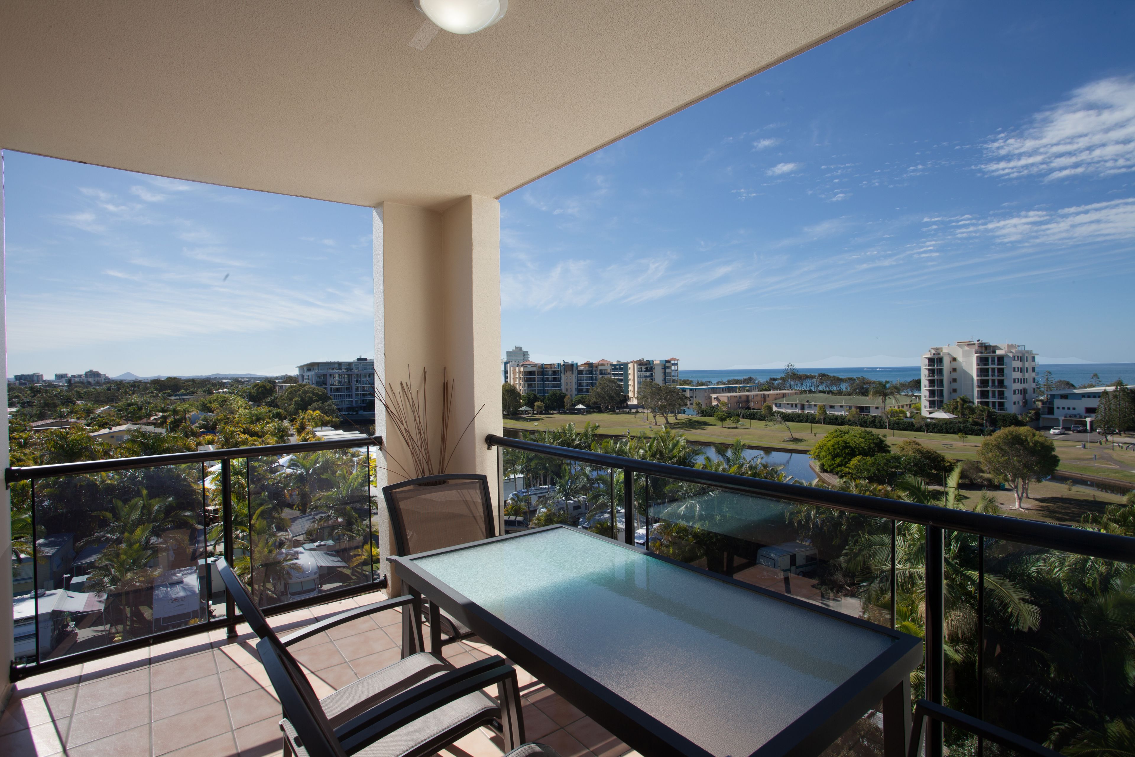 A balcony with a table and chairs, offering a view of a cityscape and a body of water.
