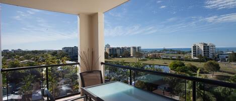 A balcony with a table and chairs, offering a view of a cityscape and a body of water.