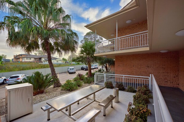A balcony with a metal table and benches, surrounded by plants and a palm tree.