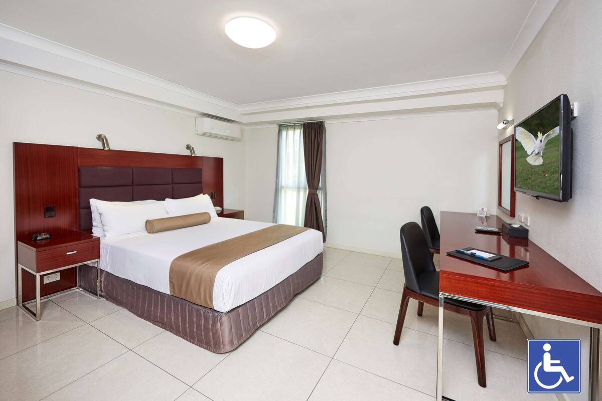 Una habitación de hotel con cama, mesita de noche, escritorio, silla y televisión.