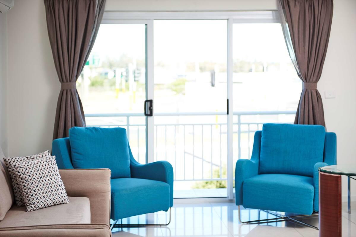 Una sala de estar moderna con dos sillones azules, un sofá color beige y un cojín estampado.