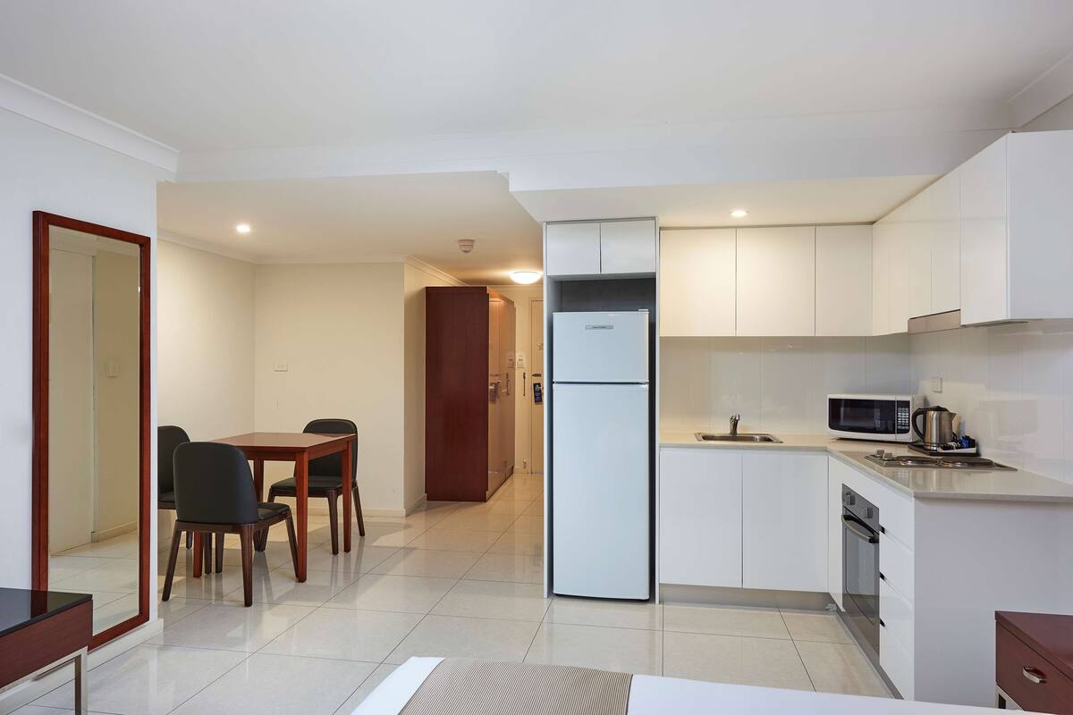 Una cocina moderna con armarios blancos, un refrigerador, un microondas y un comedor con mesa y sillas.