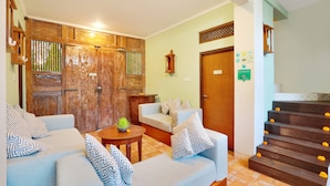 A living room with a sofa set, a wooden door, and a staircase with flower decorations. - The Vie Villa Legian (Seminyak)