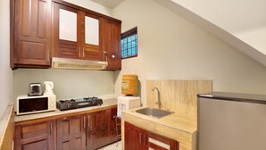 A compact kitchen with wooden cabinets, a microwave, a toaster, a sink, and a refrigerator. - The Vie Villa Legian (Seminyak)