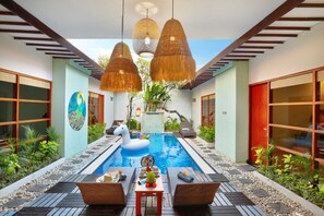 Une piscine agrémentée d’un flotteur en forme de cygne, entourée d’une terrasse en bois et de chaises en osier, avec des lampes en rotin suspendues et un jardin tropical.