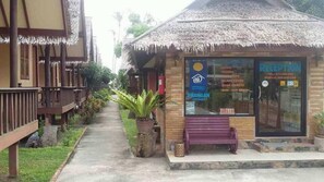 A reception area with a thatched roof, a bench, and a signboard listing services like island tours and bike rentals.