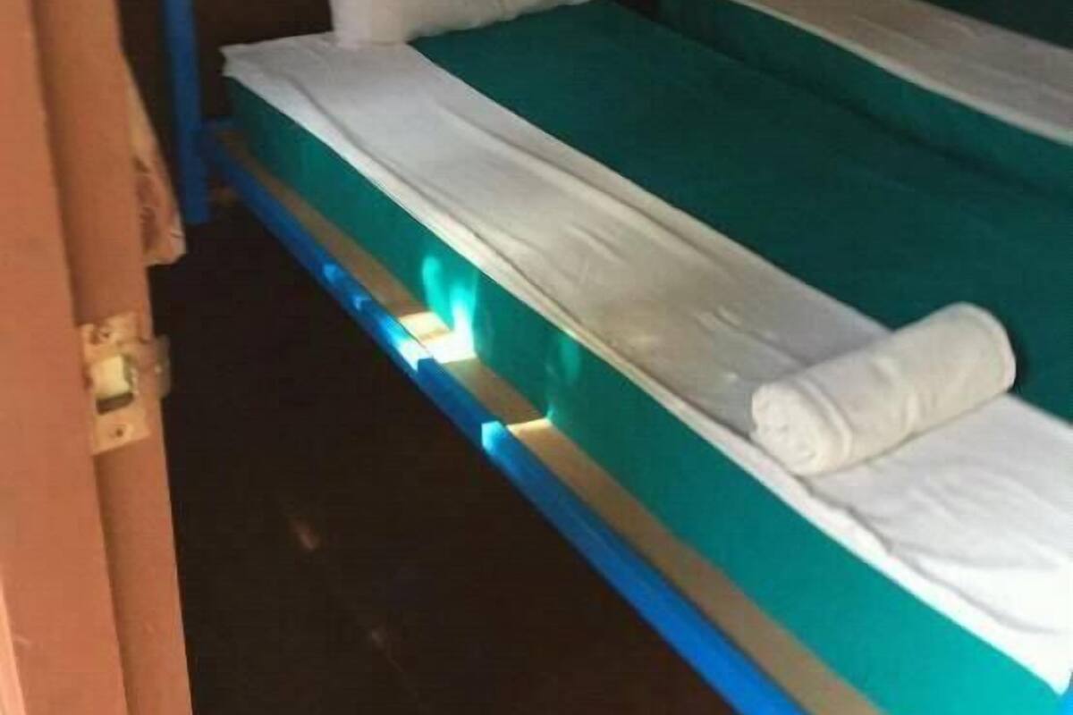 A single bed with a teal mattress and white bedding, a white pillow, and a rolled-up white towel.