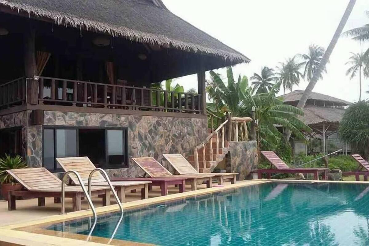 A resort with a pool, lounge chairs, and a thatched-roof building.
