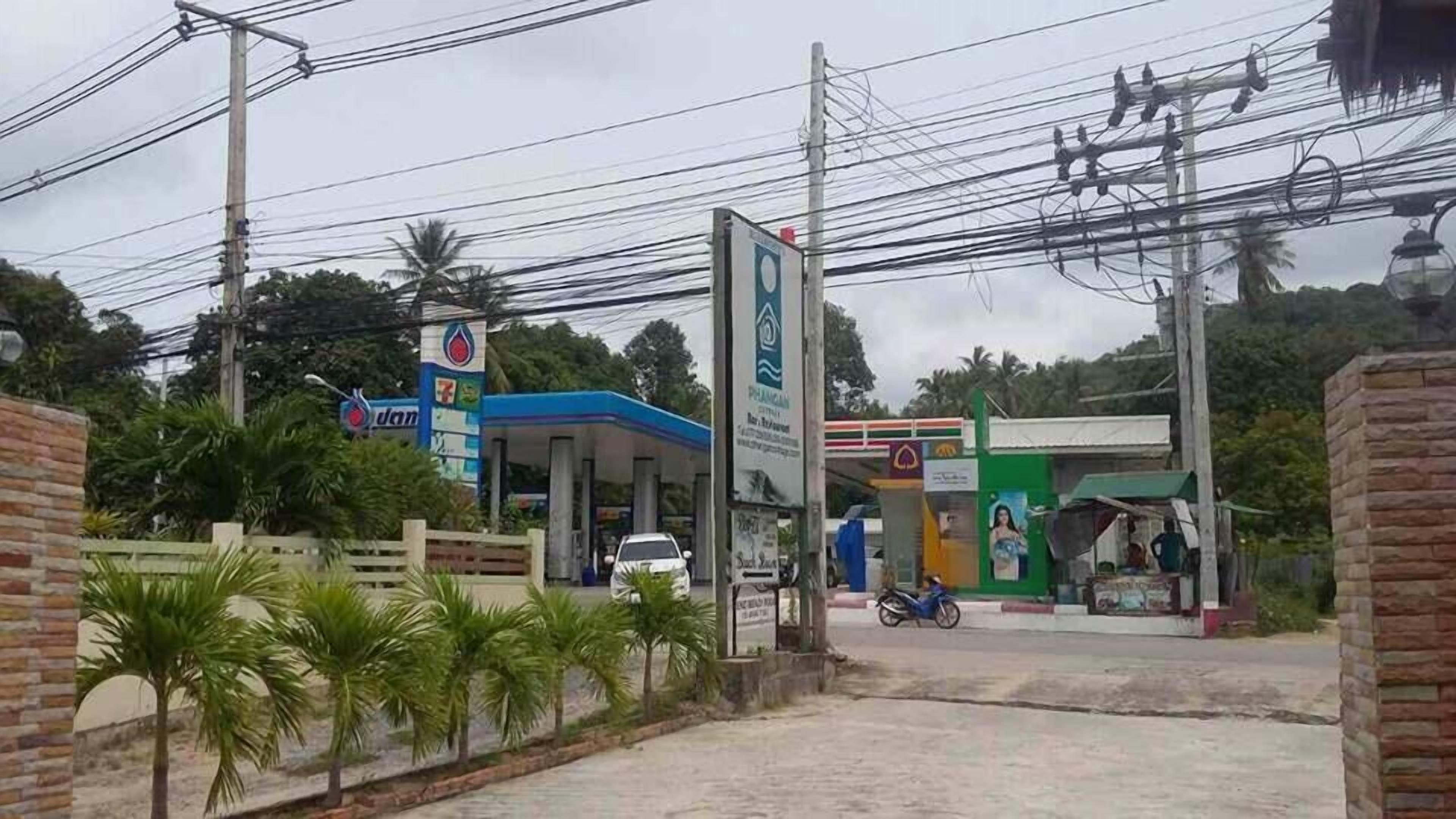 A gas station with multiple fuel pumps, a small convenience store, and a few palm trees in the foreground.