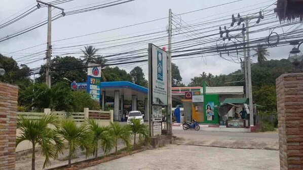A gas station with multiple fuel pumps, a small convenience store, and a few palm trees in the foreground.