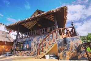 A building with a thatched roof, stone walls, and a staircase leading to a balcony.
