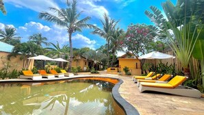 A pool area with lounge chairs and umbrellas, surrounded by palm trees and tropical plants.