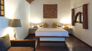 A bedroom with a large bed, wooden ceiling beams, two bedside lamps, a nightstand, and a framed picture on the wall.