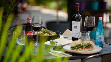 A dining table with a bottle of wine, glasses, a Coca-Cola bottle, a bowl of salad, and a sandwich.