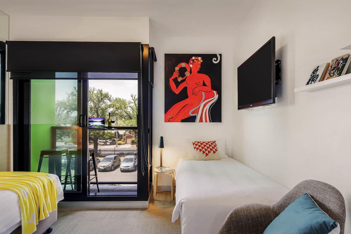 A hotel room with a bed, a sofa, a TV, a painting, and a view of the street.